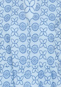 Tissu bleu clair avec des motifs floraux et circulaires brodés en bleu foncé, agrémenté de boutons recouverts de tissu le long d'un col en V.