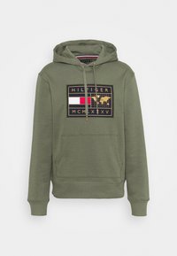 Felpa verde oliva con cappuccio, caratterizzata da un logo grafico centrale in nero, rosso e oro. Include una tasca a marsupio e polsini a coste.