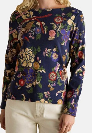 Haut bleu marine à manches longues avec des motifs floraux colorés et des oiseaux, associé à un pantalon blanc cassé, présenté du cou aux hanches.