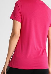 Tajtat t-shirt med kort ärm i klart rosa tyg, slät textur, rund hals och en enkel design utan synliga logotyper eller mönster.