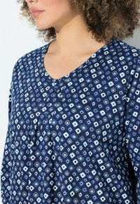 Top blu navy con scollo a V, realizzato in un morbido tessuto con un motivo geometrico a rombi in tonalità di azzurro chiaro e bianco.