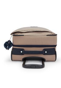 Beige matkalaukku, jossa sileä pinta, tummansinisiä yksityiskohtia, ulosvedettävä kahva ja vetoketjuun kiinnitetty karvainen tummansininen koriste.