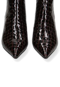 Bottes à talons hauts à bout pointu en matériau crocodile brillant de couleur marron foncé. Texture lisse, design épuré avec un talon aiguille.