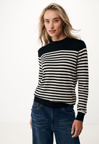 Maglione a righe nero e crema con scollatura rotonda e polsini a costine, abbinato a jeans di denim scuro. Tessuto morbido, vestibilità casual.