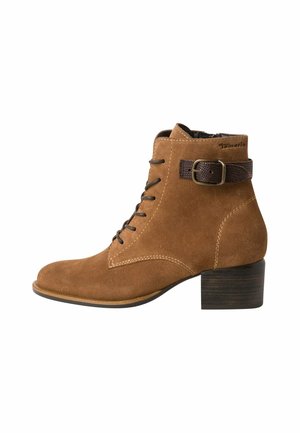 Bottine en cuir suédé marron avec un embout carré, un système de laçage à l'avant, et une sangle décorative marron avec une boucle en métal. Elle possède un petit talon carré.