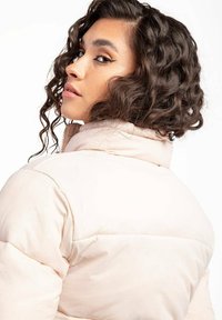 Chaqueta de plumas rosa claro con un cuello alto y diseño acolchado. La tela parece suave, con una textura lisa y acentos sutiles.