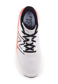 Zapatilla deportiva blanca con cordones y acentos negros, que cuenta con una parte superior de malla transpirable, superficie texturizada y suela de color coral.