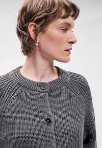 Γκρι πλεκτό cardigan με στρογγυλή λαιμόκοψη, κλείσιμο με κουμπιά και ραμμένα σημεία. Διαθέτει υφαντό σχέδιο και ράγλες μανίκια.