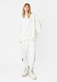 Sudadera blanca de gran tamaño con dobladillo acanalado, combinada con joggers blancos con acentos plateados en forma de hojas, y botas gruesas beige.