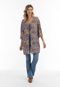 Barevný kimono vzoru paisley s polovičními rukávy, otevřeným předním dílem a zavazováním, nošené přes šedý top a spárované s světlými džíny.