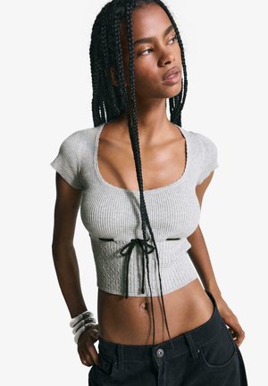 Harmaa ribbed crop-top, jossa on lyhyet hihat ja pyöreä kaula-aukko, vyötäröllä musta nyöri. Yhdistetty tummiin housuihin.