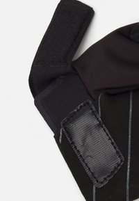 Svart hanske med neopren-kropp og borrelåsrem, teksturerte detaljer, og synlig søm. Lett design med fleksibel materiale.