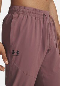 Mauve atletiske shorts lavet af letvægtsmateriale med elastisk talje og justerbar snor. Har et sort Under Armour-logo.