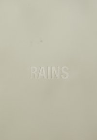 Svetlo béžový povrch s embosovaným nápisom "RAINS". Hladký, matný povrch bez ďalších vzorov alebo akcentov.