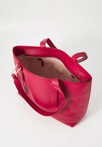 Bolsa tote de couro pebble vermelha com duas alças na parte superior e fecho com zíper. O interior apresenta forro bege com um pequeno bolso.