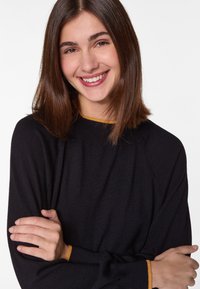 Zwarte pullovertrui met raglanmouwen, voorzien van een contrasterende mosterdkleurige afwerking bij de halslijn en manchetten, gemaakt van zachte stof.