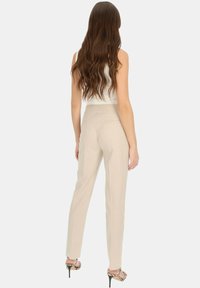 Beżowe spodnie dopasowane o wąskim kroju, z gładką fakturą i tylnymi kieszeniami, w połączeniu z sandałami na obcasie i białą bluzką.