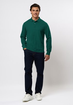 Langsleeve teal polo met drie knopen, gecombineerd met donkere jeans en witte sneakers. Soepele stof, aansluitend ontwerp.