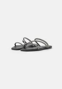 Des sandales plates noires présentent plusieurs lanières compliquées avec une surface texturée, conçues pour le confort et une couverture minimale.