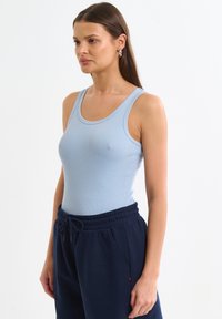 Heled sinine ribitud tank top laia õlapaelaga, koos tumesiniste stringidega treeningpükstega, millel on küljetaskud ja väike logo.