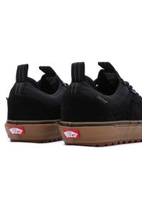 Czarne sneakersy z zamszu i materiału tekstylnego z gumową podeszwą, ozdobione białym przeszyciem, językiem do ściągania oraz czerwonymi akcentami marki na pięcie.