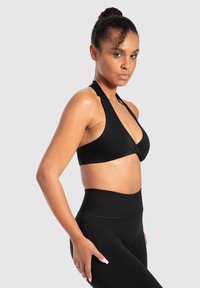 Zwarte halter-sportbeha met een gedraaide voorkant, gecombineerd met hoge zwarte leggings, beide in een gladde, rekbare stof.