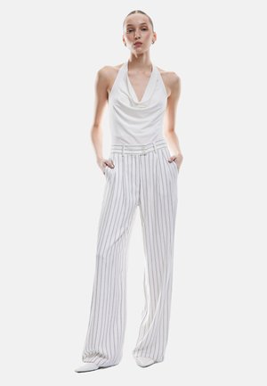 Haut à bretelles blanc avec décolleté drapé associé à un pantalon large à taille haute rayé en blanc et gris clair. Détail de bouton minimalist.
