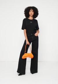 Tricou negru supradimensionat cu un logo mic, blugi negri evazați cu talie înaltă și o geantă portocalie curbată. Texturi netede și culori vii.