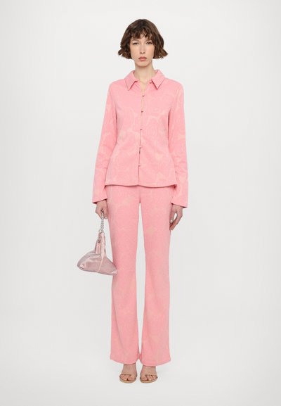 Pink floral-patterned suit jacket with matching trousers, long sleeves, and a button closure. Accessorized with a metallic handbag and sandals.