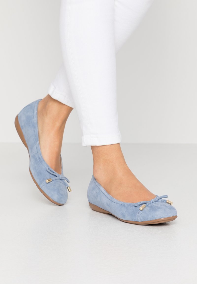 Ballerines en daim bleu clair avec un bout arrondi, ornées d'un nœud attaché et d'un petit détail en métal doré, associées à un jean blanc raccourci.