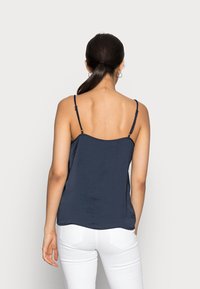 Mörkblå topp med tunna justerbara remmar och en något lös passform, tillverkad av ett slätt material, kombinerad med vita figurnära byxor.