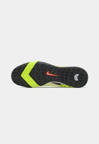 Đon od neon zelene i crne atletske cipele s teksturiranim gripom, crveni Nike swoosh logo u centru i nagibi u obliku chevrona.