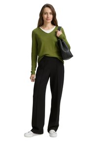 Suéter verde de cuello en V hecho de tela ligera, combinado con pantalones negros de pierna ancha. La modelo sostiene un bolso negro y lleva zapatillas blancas.