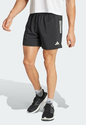 Shorts de sport noirs avec une ceinture élastique, ornés de trois bandes blanches sur le côté. À assortir avec des chaussures de course noires et des chaussettes grises.