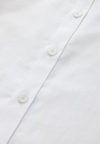 Close-up of white fabric with stitched seam and three small white buttons on a shirt or similar garment.