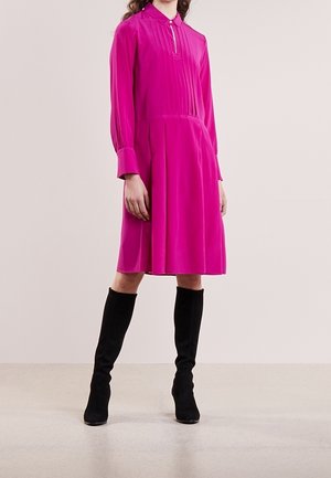 Różowa sukienka z długim rękawem, z kołnierzykiem, plisowaną fakturą i rozkloszowanym dołem. W połączeniu z czarnymi zamszowymi kozakami za kolano.