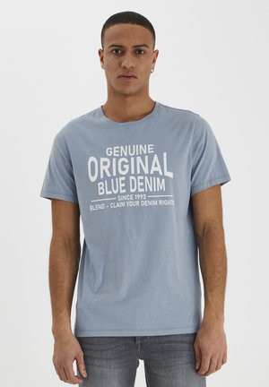Lyseblå bomull T-skjorte med en grafisk trykk i hvitt med teksten "Genuine Original Blue Denim" og slagorddetaljer nedenfor.