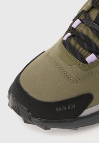 Grøn tekstilsneaker med sort gummisål, med lilla detaljer og en tekstureret overdel. "RAIN RDY" mærke på siden.