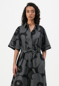 Short-sleeve dress in a patterned dark gray fabric with large black floral shapes, featuring a belted waist and button-down front.