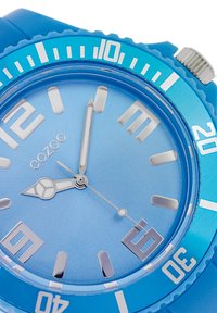 Montre en silicone bleue avec un cadran rond, des aiguilles des heures et des minutes en argent, et des chiffres en gras. Présente une lunette texturée et une finition brillante.