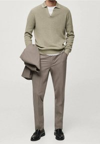 Beige trui met V-hals, gecombineerd met lichtbruine broek. Zwarte schoenen maken de outfit compleet. Gladde textuur, minimalistisch ontwerp, zonder patronen.