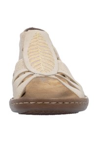 Sandale beige avec des lanières découpées et un design de feuille en broderie dorée sur le devant. Matériau doux et semelle marron avec un détail de couture.