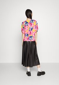 Blusa floral com mangas curtas bufantes em amarelo, rosa e azul. Saia preta plissada. Sapatos pretos com solas grossas. Meias brancas visíveis.