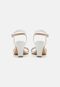 Weiße High-Heelsandalen mit einer glatten Lederoberfläche, offener Ferse und Knöchelriemen, ausgestattet mit einem moderaten Blockabsatz und einer weichen beigen Innensohle.