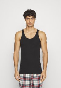 Débardeur noir au design ajusté, en coton, avec de larges bretelles et un col rond, accompagné de pantalons de pyjama à carreaux.