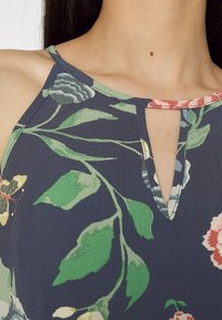 Blusa com padrão floral, apresentando um fundo azul escuro, folhas verdes e flores coloridas, com decote em gota e tecido texturizado.