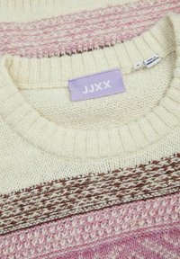 Gebreide trui met crème, roze en bruine strepen. Zachte textuur met geribbelde halslijn en zoom. Etiket leest "JJXX," gemaakt in Bangladesh.