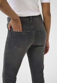 Jean en denim gris avec un design ajusté, taille mi-haute et deux poches arrière. La texture est lisse avec des détails de couture subtils.