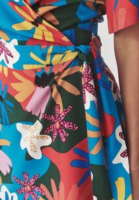 Monivärinen kukkamekko kietaisumallilla, jossa on suuria, rohkeita kuvioita sinisellä, vihreällä ja punaisella taustalla. Pehmeä kangas.