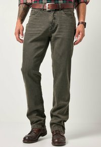 Pantaloni dritti color verde oliva realizzati in tessuto resistente, dotati di cinque tasche e dettagli in metallo, abbinati a stivali in pelle marrone.